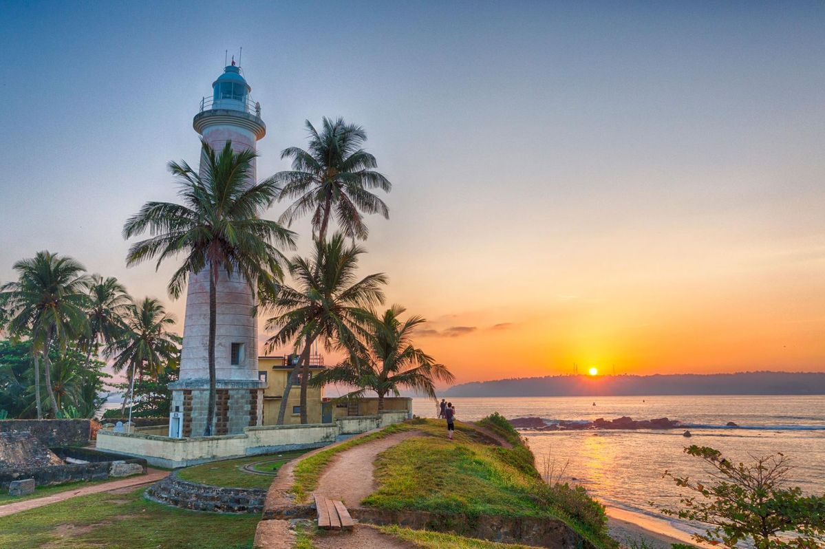 Galle Fort lighthouse framed by palm trees at sunset